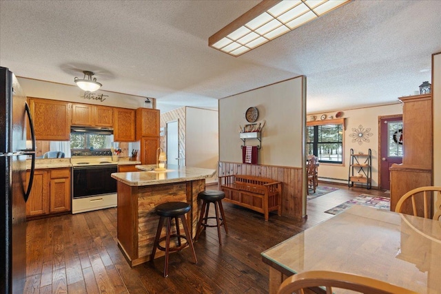 kitchen featuring dark wood-type flooring, a breakfast bar, sink, black fridge, and electric range