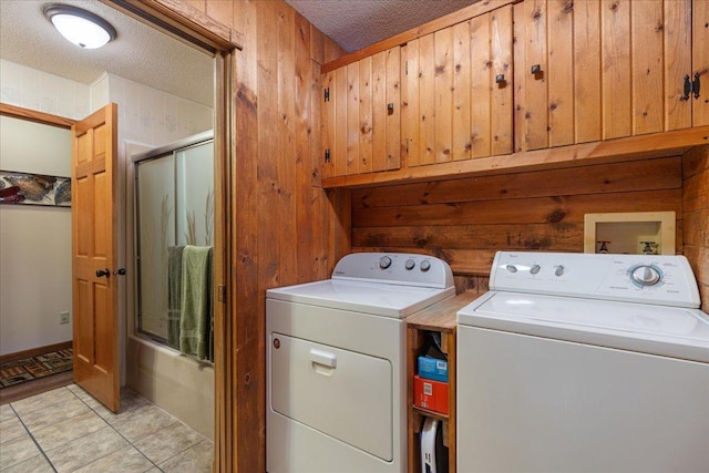 laundry room with light tile patterned floors, wooden walls, cabinets, a textured ceiling, and washing machine and clothes dryer