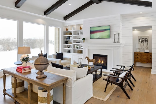 living room featuring a fireplace, lofted ceiling with beams, light hardwood / wood-style floors, and built in features