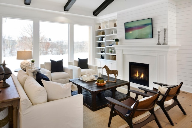 living room featuring a fireplace, light wood-type flooring, and beamed ceiling