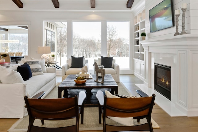 living room with beamed ceiling, built in shelves, light hardwood / wood-style floors, and a wealth of natural light