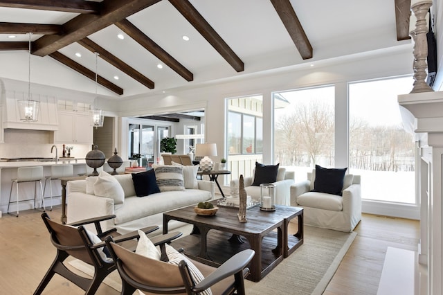 living room featuring vaulted ceiling with beams, light hardwood / wood-style floors, an inviting chandelier, and sink