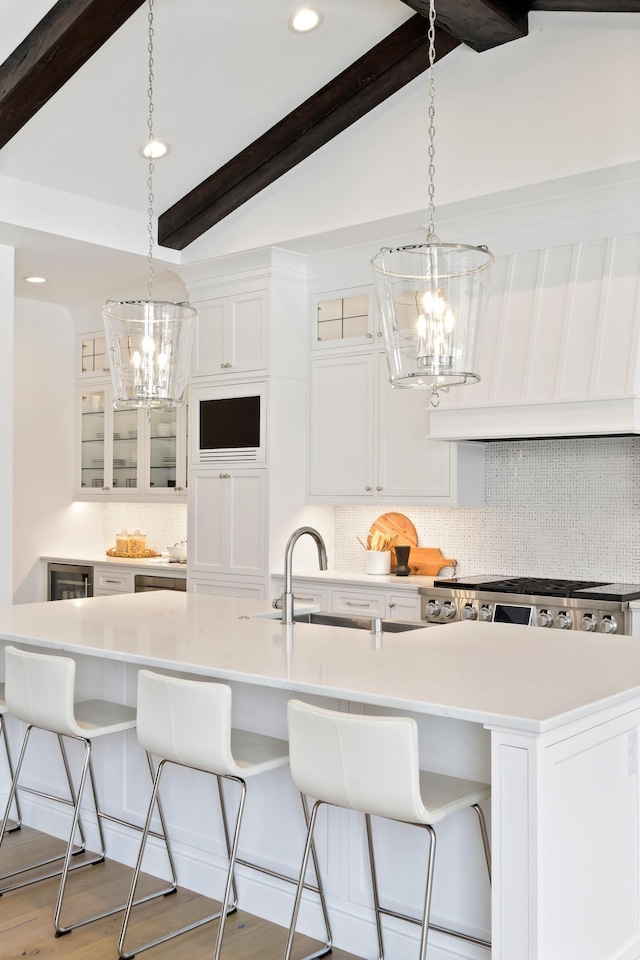 kitchen featuring lofted ceiling with beams, a large island with sink, pendant lighting, a breakfast bar, and light wood-type flooring