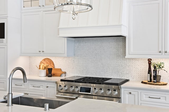 kitchen featuring backsplash, high end stainless steel range oven, sink, white cabinets, and a chandelier