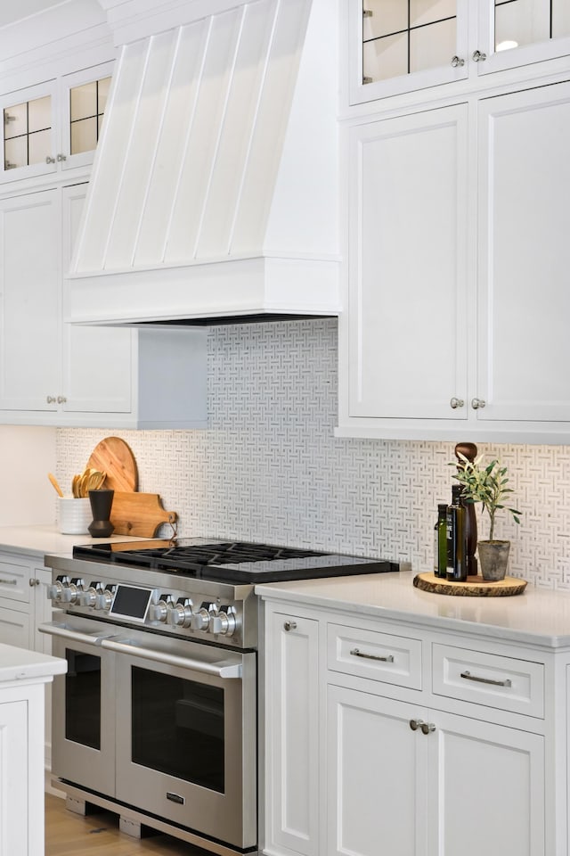 kitchen with tasteful backsplash, range with two ovens, white cabinets, custom exhaust hood, and light wood-type flooring