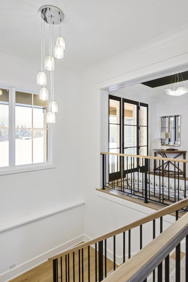 stairs featuring plenty of natural light, wood-type flooring, crown molding, and an inviting chandelier