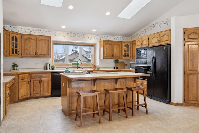 kitchen with a kitchen island, vaulted ceiling with skylight, sink, a kitchen breakfast bar, and black appliances