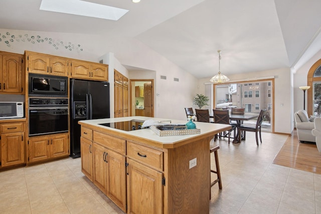 kitchen with lofted ceiling with skylight, light tile patterned flooring, decorative light fixtures, a center island, and black appliances