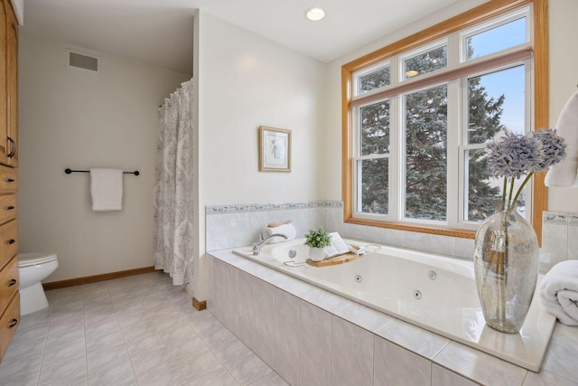 bathroom with tile patterned flooring, tiled bath, and toilet