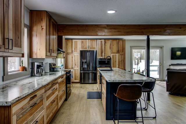 kitchen featuring a breakfast bar area, light wood-style floors, black appliances, brown cabinetry, and a center island with sink