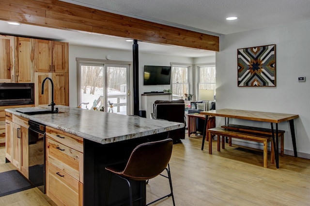 kitchen with black microwave, a kitchen island with sink, open floor plan, light countertops, and light wood finished floors