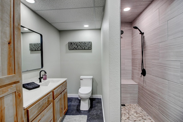 full bathroom featuring toilet, baseboards, tiled shower, and vanity