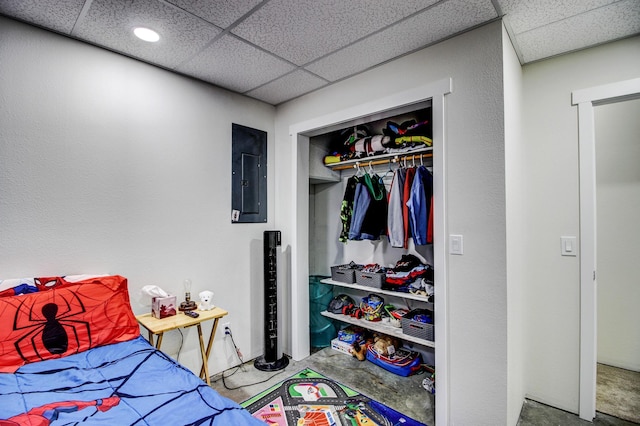 bedroom with a paneled ceiling, electric panel, unfinished concrete floors, and a closet