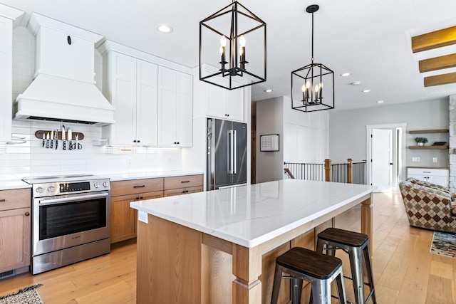 kitchen featuring a center island, appliances with stainless steel finishes, premium range hood, white cabinetry, and decorative light fixtures