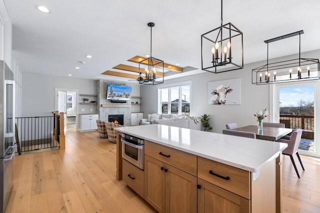 kitchen with decorative light fixtures, light wood-type flooring, a stone fireplace, and plenty of natural light