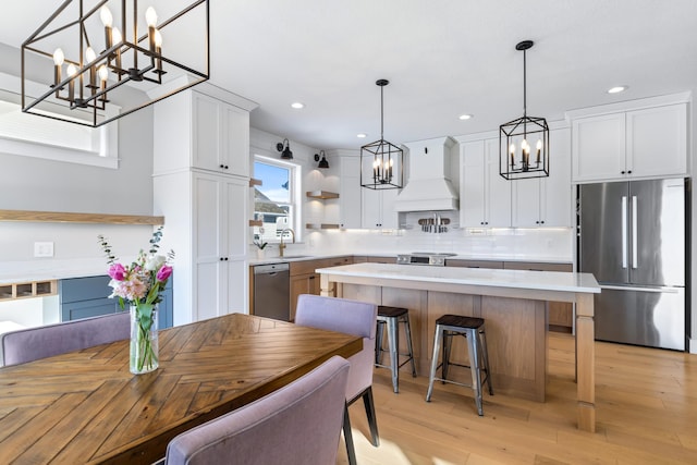 kitchen with a center island, custom range hood, white cabinets, decorative light fixtures, and stainless steel appliances