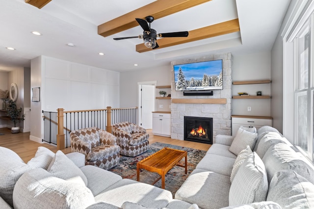 living room with light wood-type flooring, beamed ceiling, a tray ceiling, and a stone fireplace