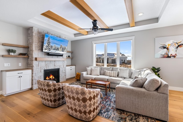 living room with ceiling fan, a raised ceiling, light hardwood / wood-style flooring, and a fireplace