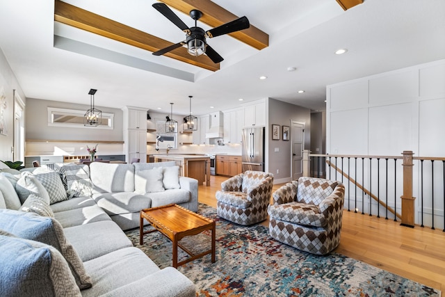 living room with ceiling fan with notable chandelier, beam ceiling, and light wood-type flooring