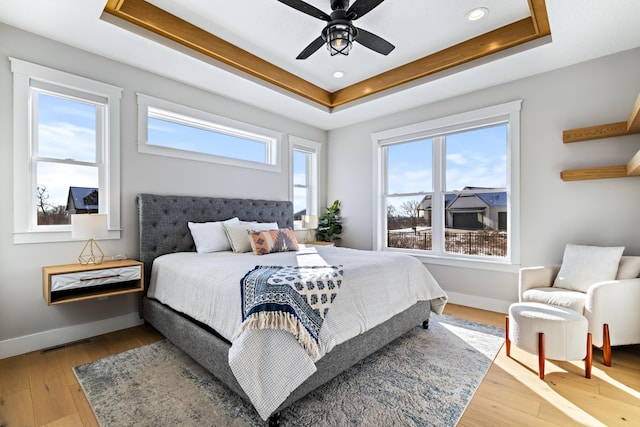 bedroom featuring light wood-type flooring, ceiling fan, and a raised ceiling