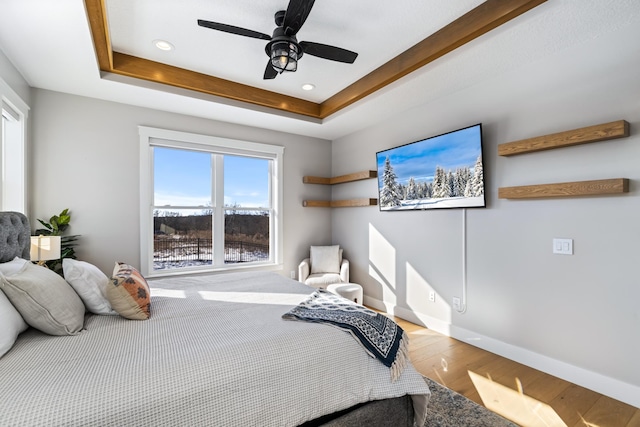 bedroom with ceiling fan, wood-type flooring, and a raised ceiling