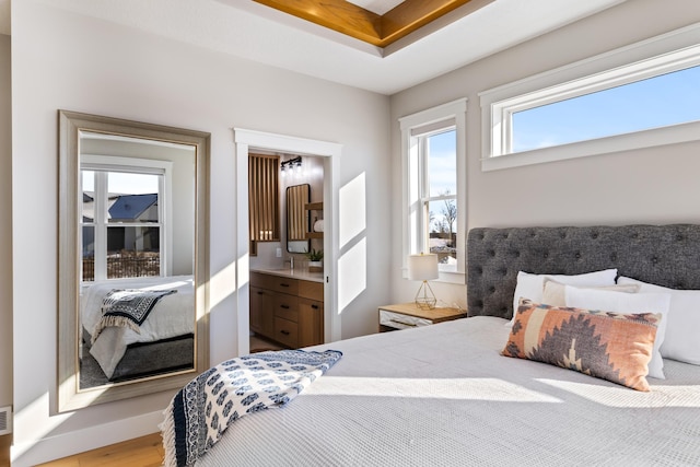 bedroom with hardwood / wood-style flooring, a tray ceiling, and ensuite bath