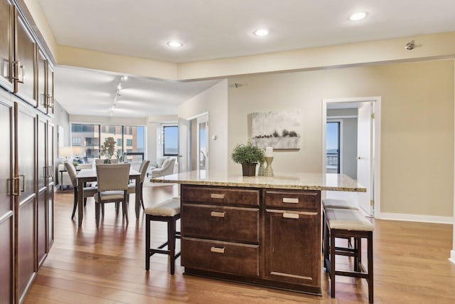 kitchen featuring dark brown cabinets, a kitchen breakfast bar, a center island, and light stone countertops