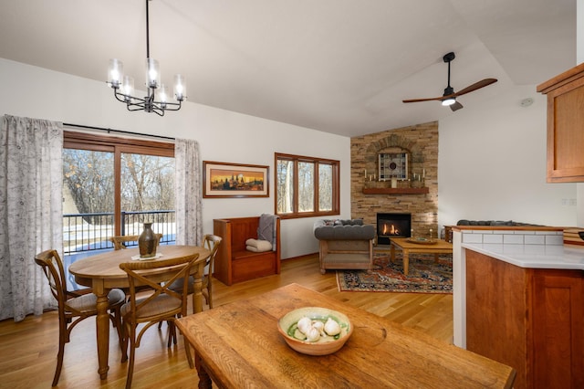 dining space featuring vaulted ceiling, a fireplace, a healthy amount of sunlight, light wood-type flooring, and ceiling fan with notable chandelier