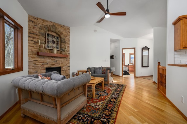 living room with ceiling fan, vaulted ceiling, a fireplace, and light hardwood / wood-style flooring