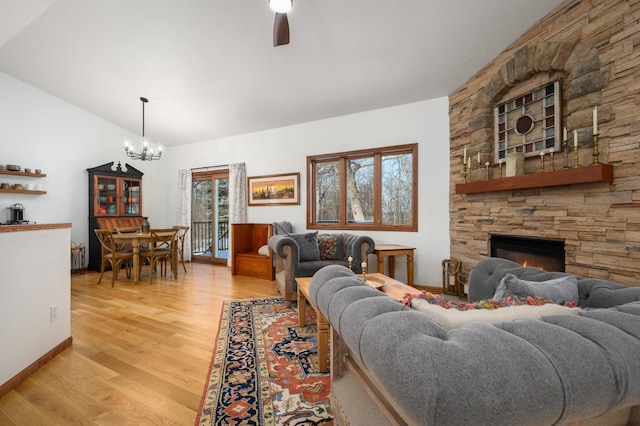 living room featuring lofted ceiling, ceiling fan with notable chandelier, a stone fireplace, and light hardwood / wood-style flooring