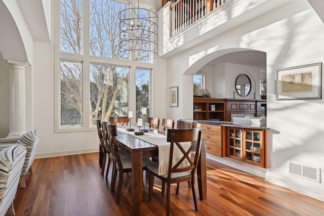 dining area featuring dark wood-type flooring, a notable chandelier, a high ceiling, and decorative columns