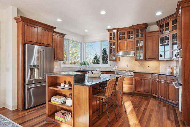 kitchen with a center island, dark hardwood / wood-style flooring, stainless steel appliances, dark stone counters, and decorative backsplash