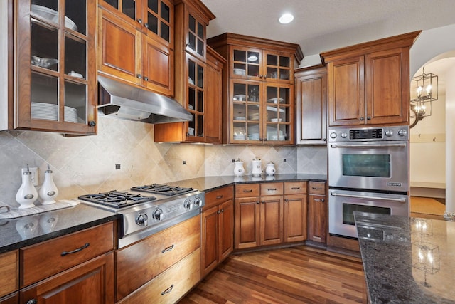 kitchen with appliances with stainless steel finishes, dark stone countertops, dark hardwood / wood-style flooring, and tasteful backsplash