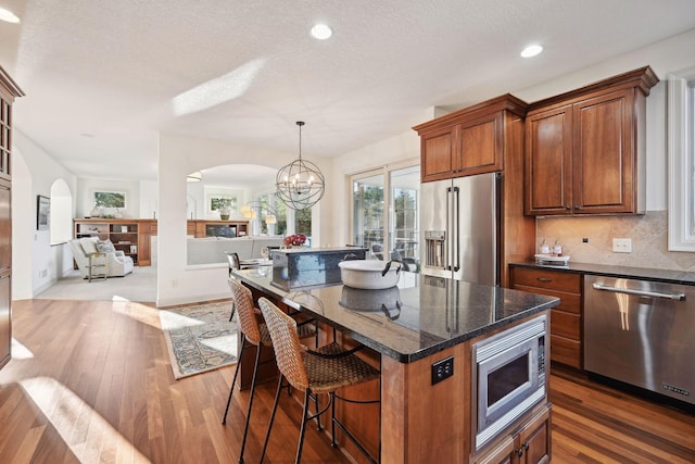 kitchen featuring decorative light fixtures, a notable chandelier, a center island, stainless steel appliances, and dark stone counters