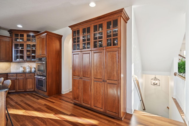 kitchen with dark hardwood / wood-style floors, double oven, tasteful backsplash, and a notable chandelier