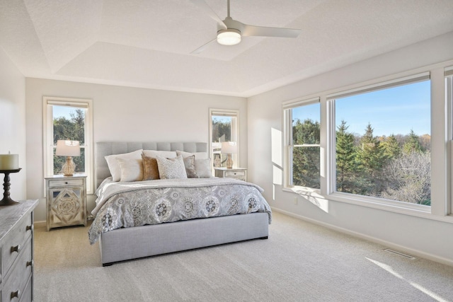 bedroom featuring light carpet, ceiling fan, a raised ceiling, and multiple windows