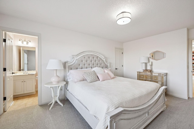 bedroom with a textured ceiling, ensuite bathroom, light colored carpet, and sink