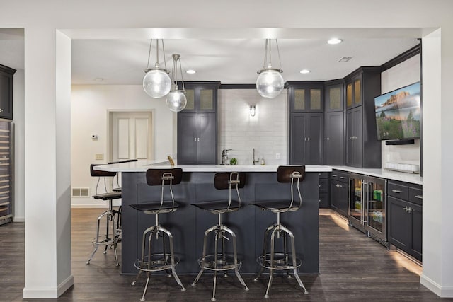 kitchen with decorative light fixtures, a breakfast bar, dark hardwood / wood-style flooring, and a center island with sink