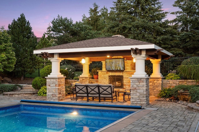 pool at dusk with a patio area, a gazebo, and an outdoor living space with a fireplace