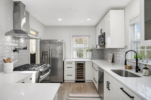 kitchen featuring wall chimney range hood, stainless steel appliances, beverage cooler, and white cabinets