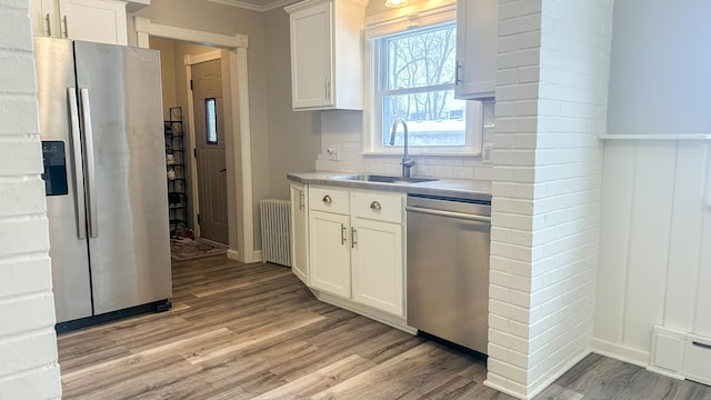 kitchen featuring a sink, stainless steel appliances, radiator, light wood finished floors, and decorative backsplash