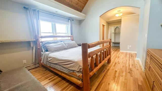 bedroom featuring a baseboard heating unit, arched walkways, light wood-style floors, and vaulted ceiling