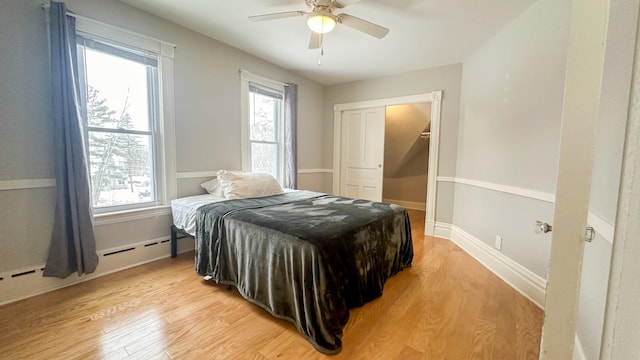 bedroom featuring a baseboard radiator, baseboards, light wood-style floors, and a ceiling fan