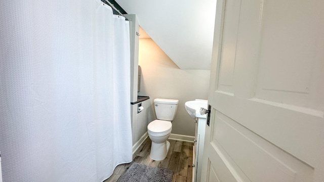 full bathroom featuring toilet, a sink, wood finished floors, baseboards, and vaulted ceiling