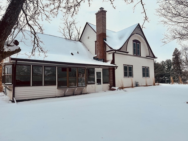 snow covered house with a chimney and a sunroom