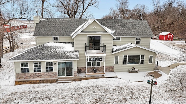 snow covered back of property with a balcony and a storage shed