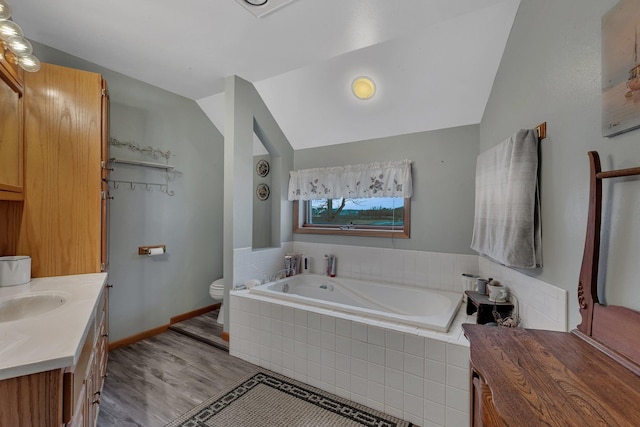 bathroom featuring vaulted ceiling, hardwood / wood-style floors, vanity, toilet, and tiled tub