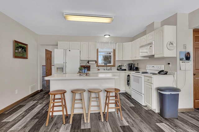 kitchen featuring a breakfast bar, white cabinetry, sink, a center island, and white appliances