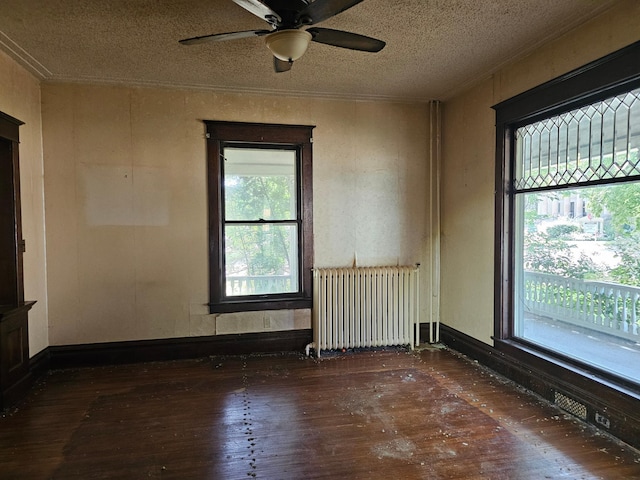 empty room with a healthy amount of sunlight, radiator heating unit, dark hardwood / wood-style floors, and a textured ceiling