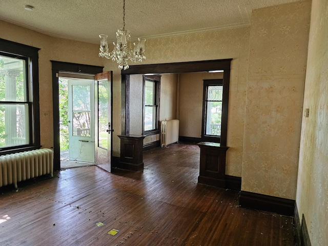 unfurnished dining area with radiator, dark wood-type flooring, a textured ceiling, and a notable chandelier